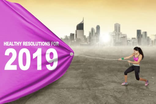 Young woman wearing sportswear while pulling banner with text of healthy resolutions for 2019. Shot with city background